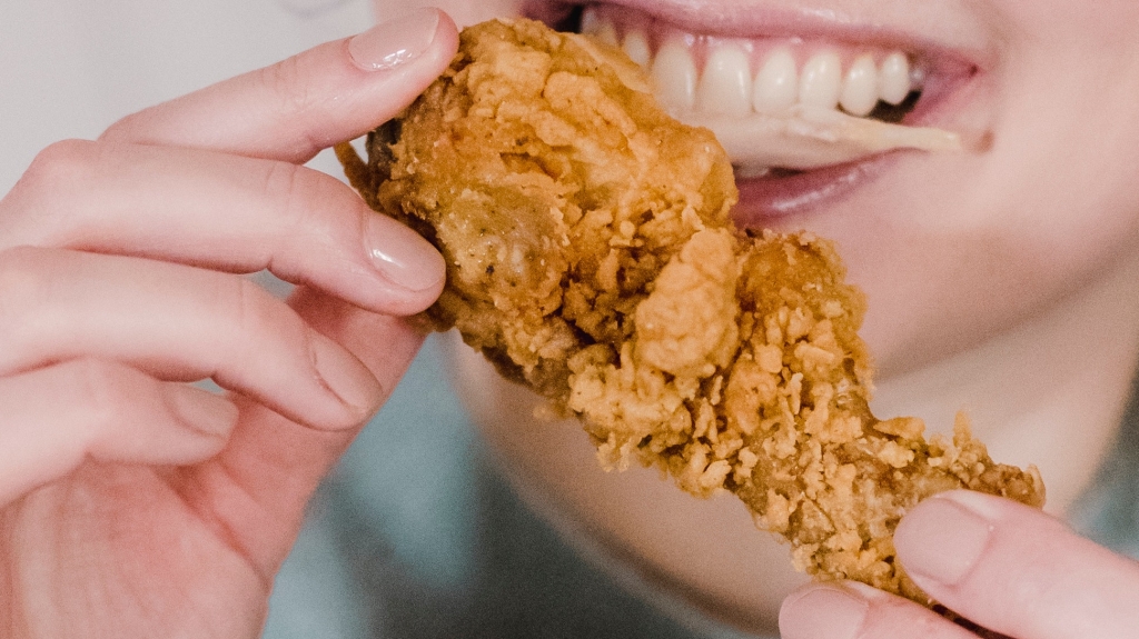 Woman biting into a piece of fried chicken.